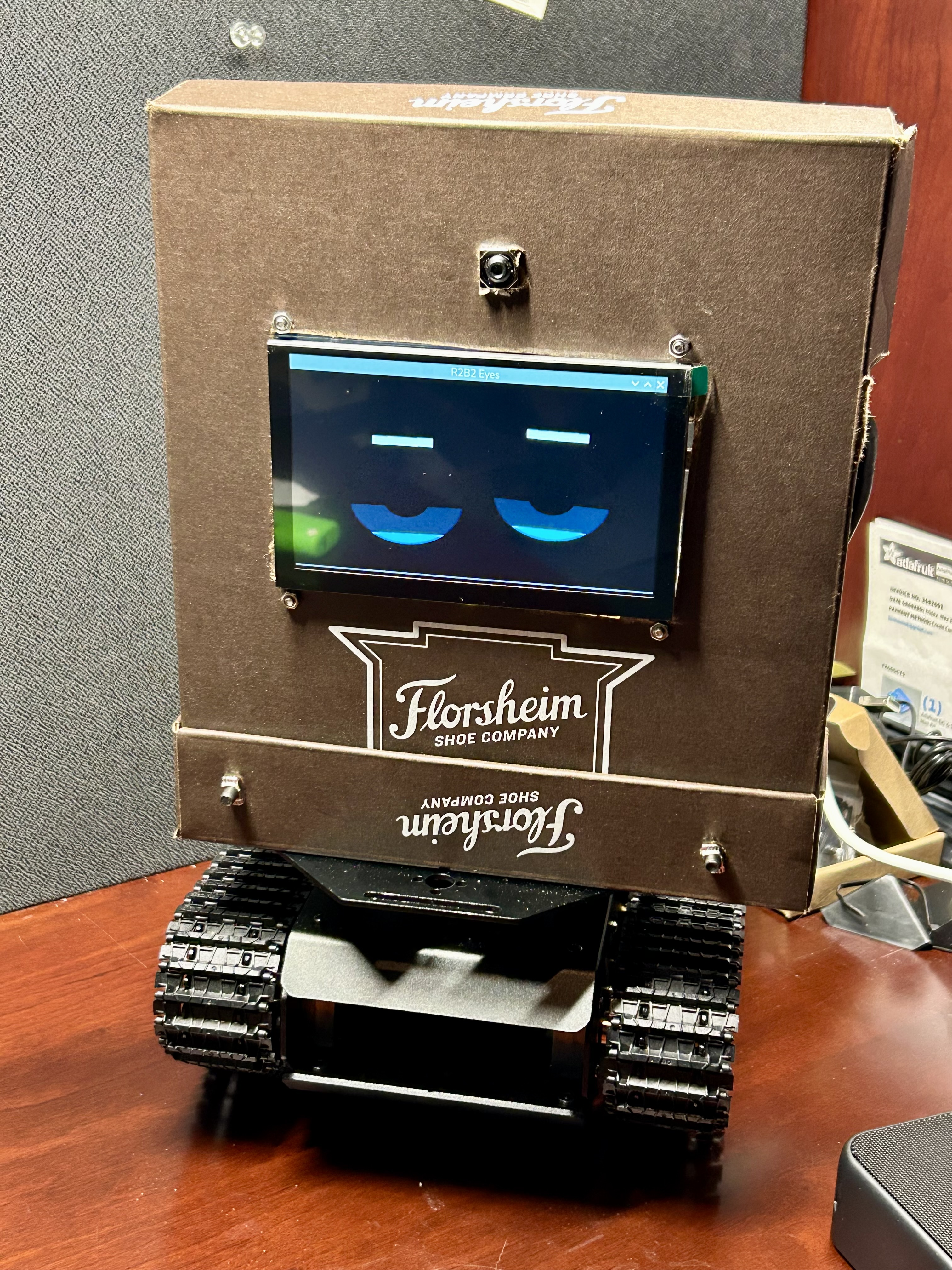 R2B2 robot with LCD eyes, pi camera, and tank tread chassis sitting on a desk